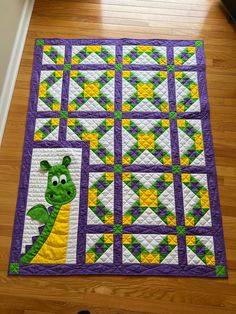 a purple and yellow quilt with a green dragon in the center on a wooden floor