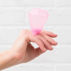 a hand holding a pink object in front of a white brick wall