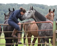 a woman leaning over a fence to kiss the nose of a horse in front of other horses