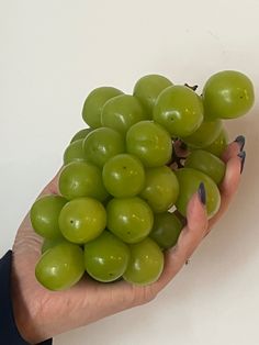 a person holding a bunch of green grapes in their hand with the other hand on top of them