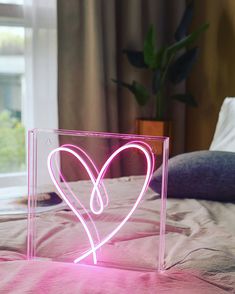 a heart shaped neon light sitting on top of a bed