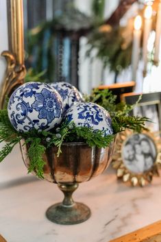 three blue and white ornaments are in a silver bowl on a marble table with greenery