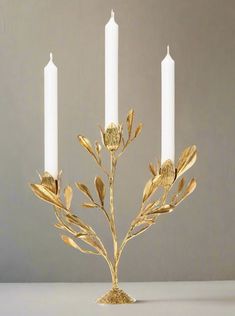 three white candles with gold leaves on them and one candle is lit in the middle