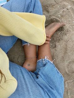 two people sitting in the sand with their feet crossed and one person has her foot up