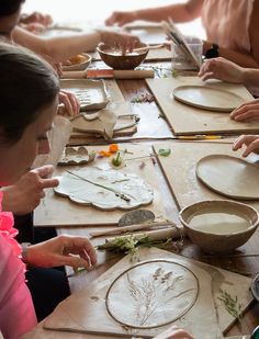 a group of people sitting around a wooden table making plates with flowers and leaves on them