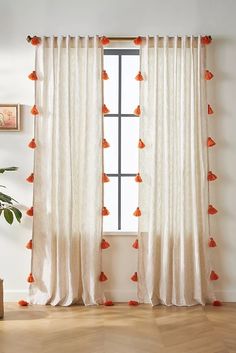 a white curtain with orange pom poms hanging from it's side in front of a window