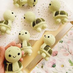 a hand is holding some little crocheted turtle figurines on a table