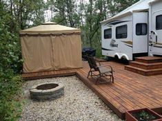 a camper trailer is parked next to a deck with chairs and a fire pit