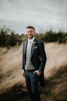 a man wearing a suit and tie standing in front of tall grass