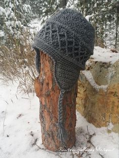 a knitted hat sitting on top of a tree stump in the snow next to some trees