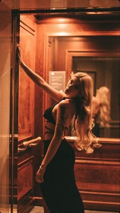 a woman in a black dress leaning against a glass door with her hand on the wall