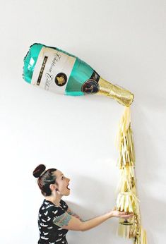 a woman holding a bottle of champagne and streamers in front of her face as she reaches for it