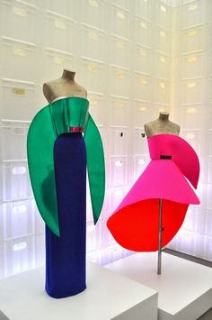 two mannequins with colorful dresses on display in front of a white wall