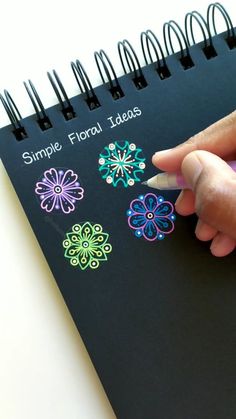 someone is drawing flowers on a black notebook