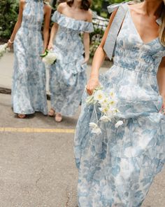 two women in blue dresses walking down the street with white flowers on their bouquets