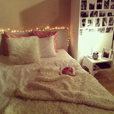 a white bed topped with lots of pillows next to a wall covered in pictures and lights