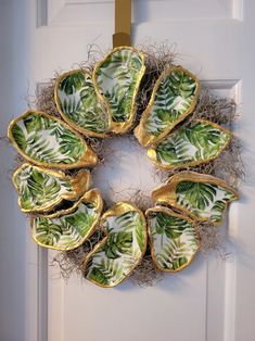 a wreath made out of green leafy dishes hanging on a white door with gold trim