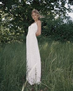 a woman standing in tall grass wearing a white dress