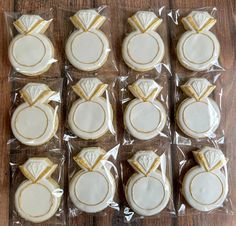 twelve decorated cookies in plastic wrappers on a wooden table with white frosting and gold trimmings