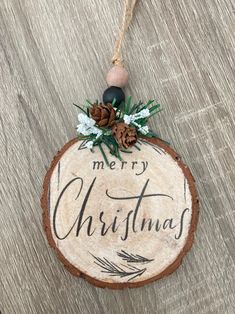 a wooden christmas ornament with pine cones and greenery hanging from a string