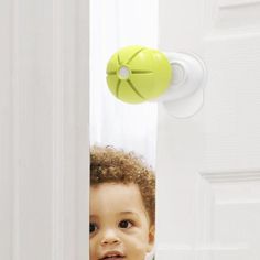 a little boy peeking out from behind a door with a green ball on the handle