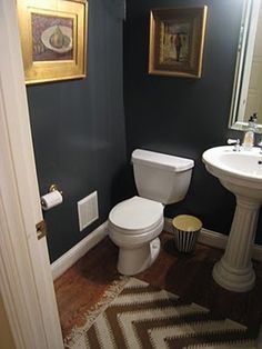 a white toilet sitting next to a sink in a bathroom under a framed painting on the wall