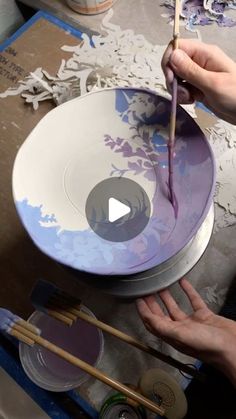 a person is painting on a bowl with paintbrushes