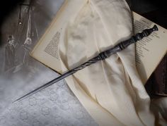 an old harry potter wand on top of an open book next to a white cloth