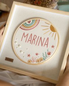 a person holding a cross stitch kit with the word marina on it