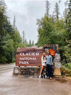 a man and woman standing next to a sign for glacier national park with their dog