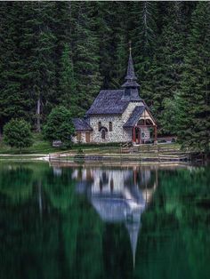 an old church sits on the shore of a lake surrounded by pine trees and evergreens