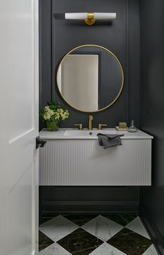 a black and white bathroom with a round mirror on the wall above the sink, gold faucet