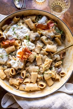 a pan filled with pasta and bacon on top of a table next to silverware