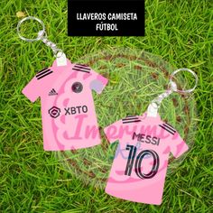 two key chains that are sitting in the grass with soccer jerseys on them, and one is