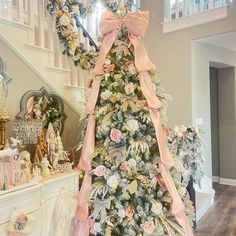 a decorated christmas tree with pink and gold bows on it in front of a staircase