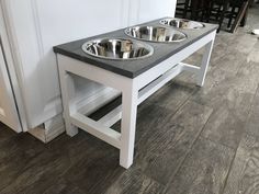 two metal bowls sit on top of a white table next to a dog bowl stand