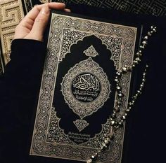 a person holding an open book with arabic writing on the cover and rosarys around it