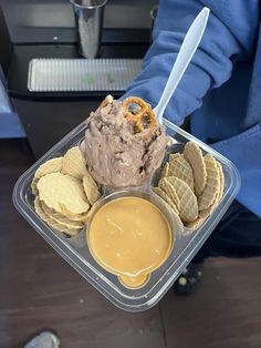 a person holding a plastic container filled with ice cream and waffles covered in peanut butter