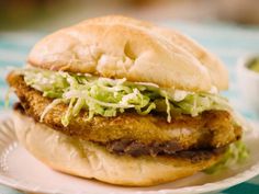 a fried chicken sandwich with lettuce and mayonnaise on a paper plate