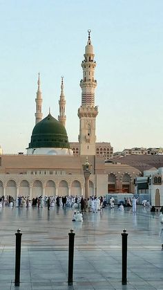 many people are walking around in front of a large building with green dome and white walls