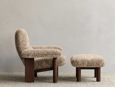 an upholstered chair and footstool in front of a gray wall with a white rug