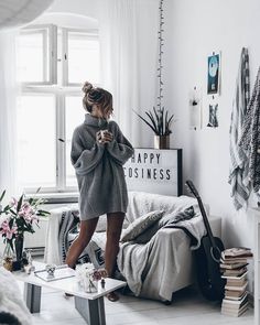 a woman standing in her living room looking at her cell phone while wearing a sweater dress