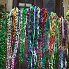 beads hanging from a gate in front of a house with green plants and shrubbery