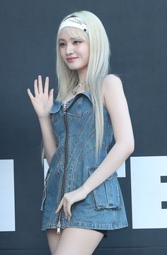 a young woman with long blonde hair wearing a denim dress and holding her hand up in the air