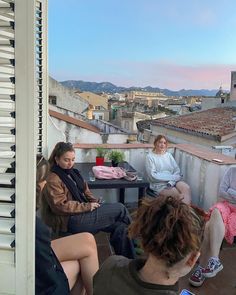 four people sitting on the roof of a building talking to each other and one person holding a cell phone