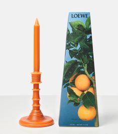 an orange colored candle stands next to a box of loewe candles