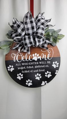 a welcome sign hanging from the side of a door with paw prints and leaves on it