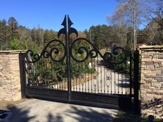 an iron gate in front of a brick wall and stone fence with trees behind it