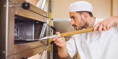 a man in a chef's hat is pulling something out of an oven with a wooden stick