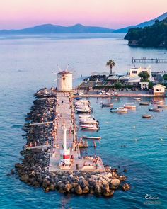 a pier with boats and people on it next to the water in front of an island